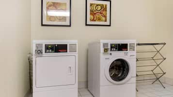 Two stacked washers and dryers in a laundry room with tiled floors and two framed abstract paintings on the wall.