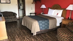 Una habitación de hotel con una cama, dos mesitas de noche, un aparador de madera, un sofá y un espejo.