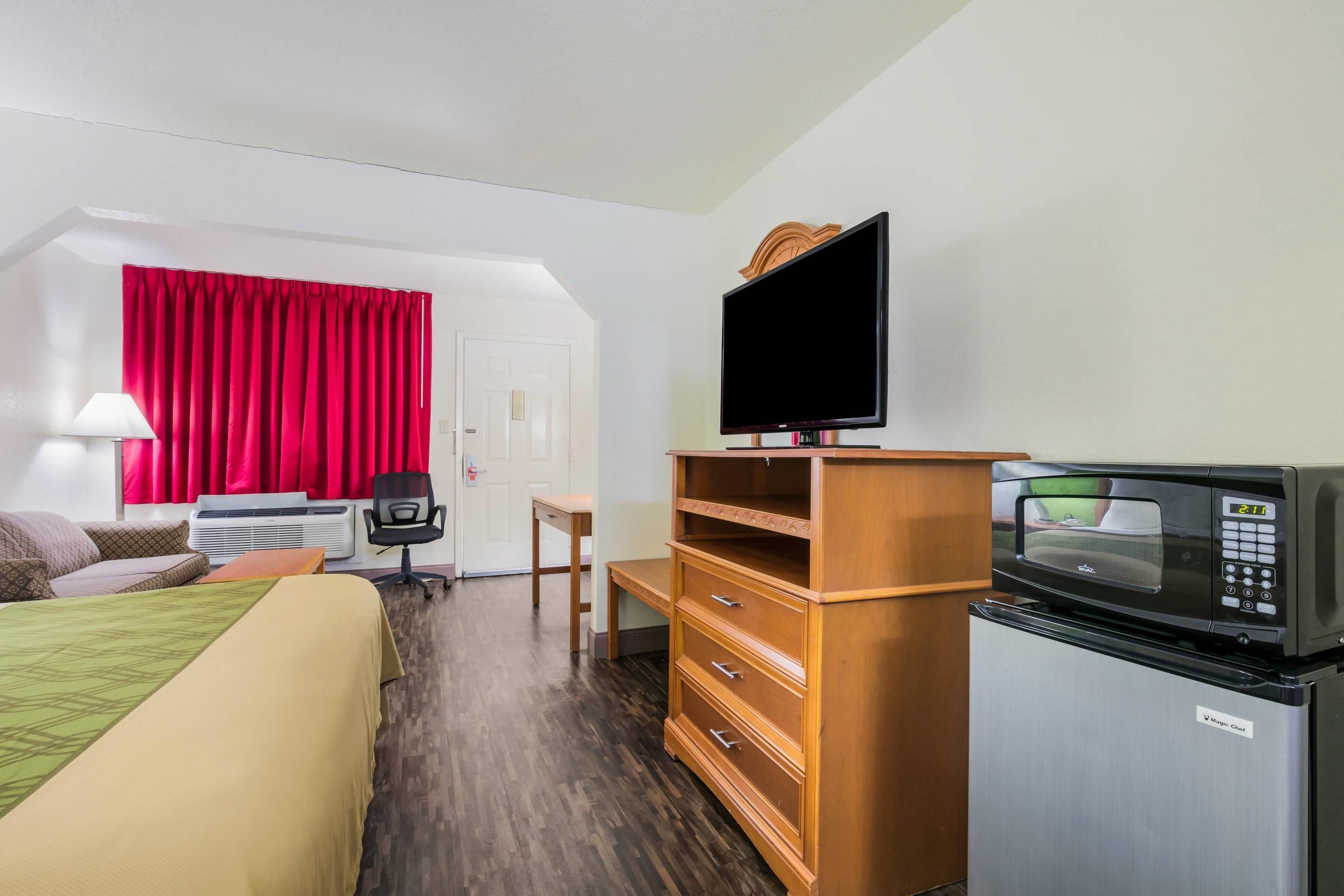 Habitación de hotel con cama, escritorio, silla, televisión, microondas y cortina roja.