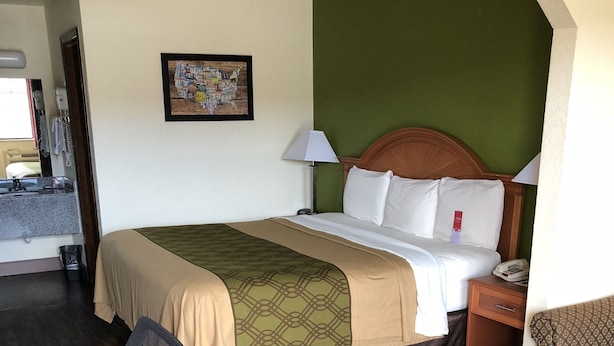 Una habitación de hotel con cama, escritorio, silla, mesita de noche y lámpara.