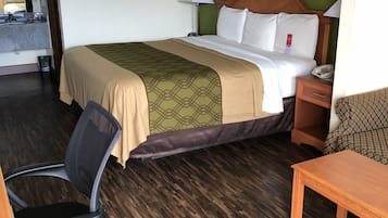 A hotel room with a bed, a desk, a chair, a nightstand, and a lamp.