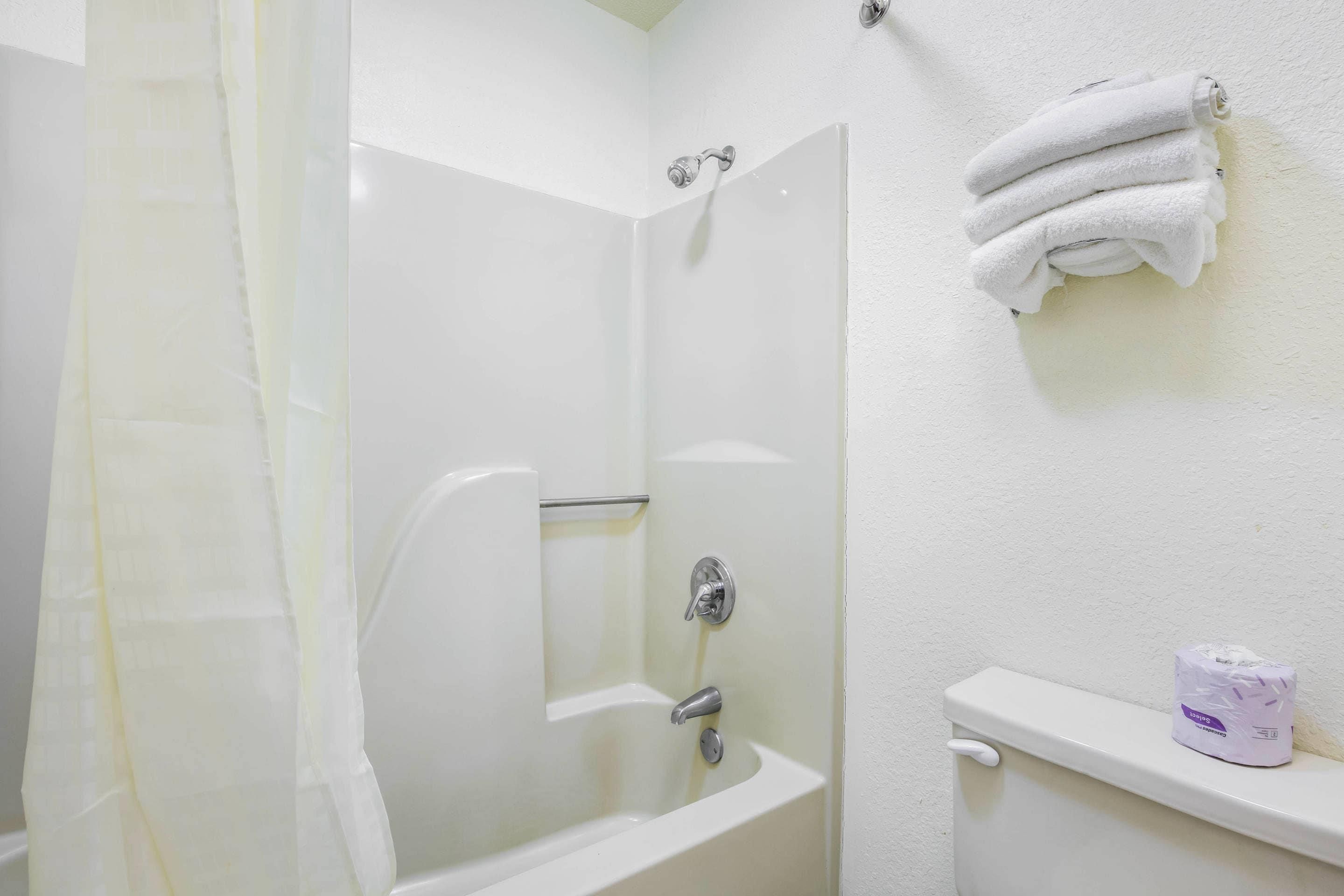 A bathroom with a bathtub, a shower curtain, a towel rack with towels, and a toilet paper dispenser.