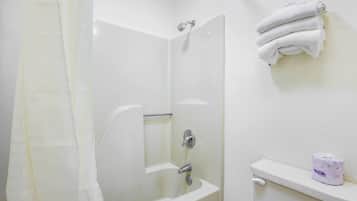 A bathroom with a bathtub, a shower curtain, a towel rack with towels, and a toilet paper dispenser.