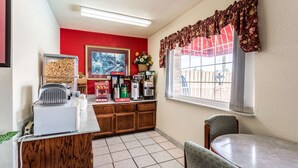 Una cocina con pared de acento roja, una cafetera, un tostador y una ventana con un valance decorativo.