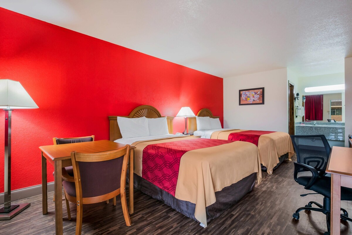 A hotel room with two beds, a desk, a chair, and a bathroom visible in the background.