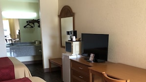 Una habitación de hotel con dos camas, un escritorio con televisor, cafetera y un cesto de basura.