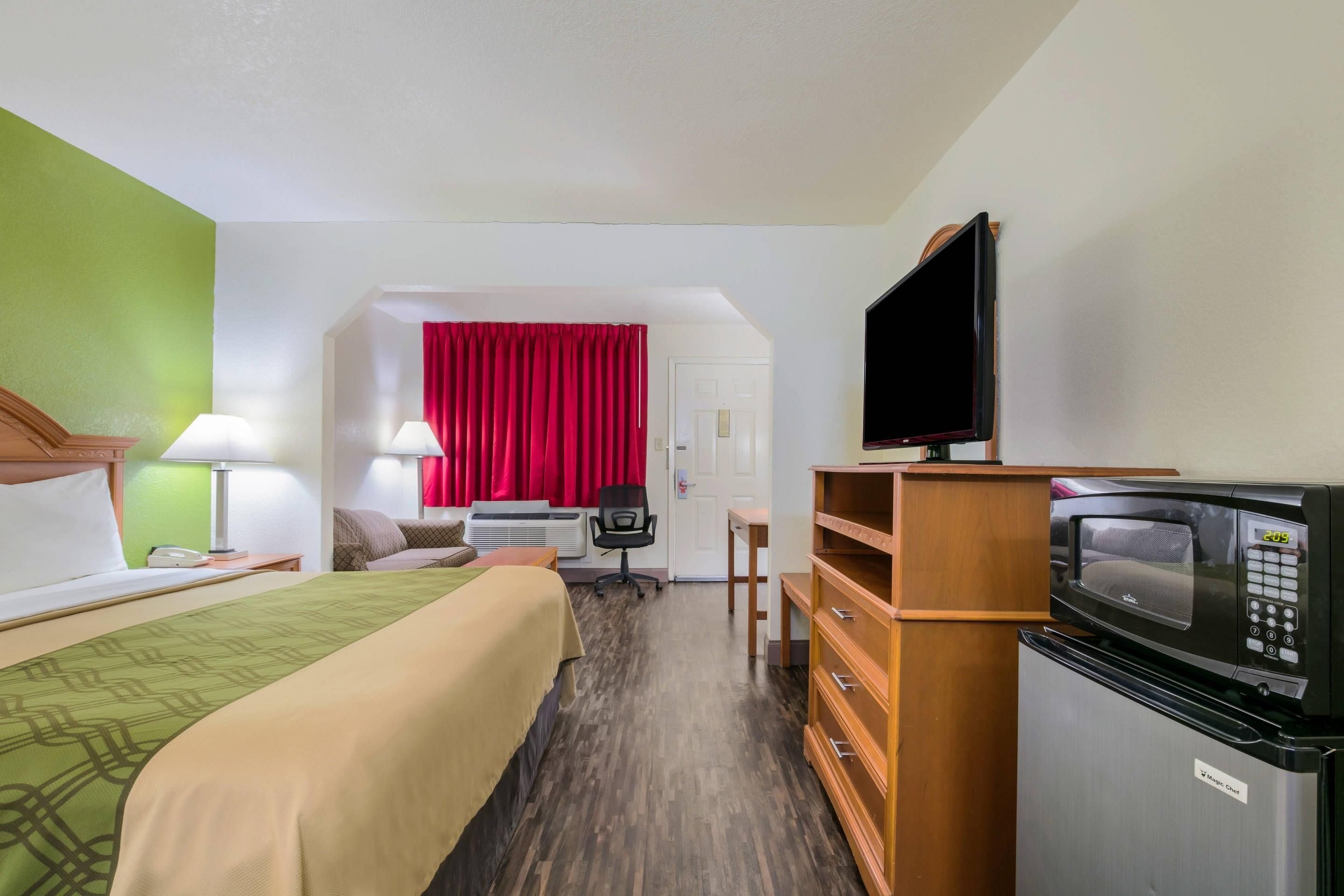 A hotel room with a bed, a desk, a television, a microwave, and a red curtain.