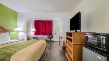 A hotel room with a bed, a desk, a television, a microwave, and a red curtain.