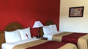 Habitación de hotel con dos camas, cabecera de madera, pared roja, suelo de madera y una mesita.