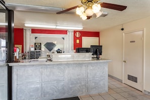 A hotel reception area with a marble counter, a clock on the wall, and a ceiling fan.