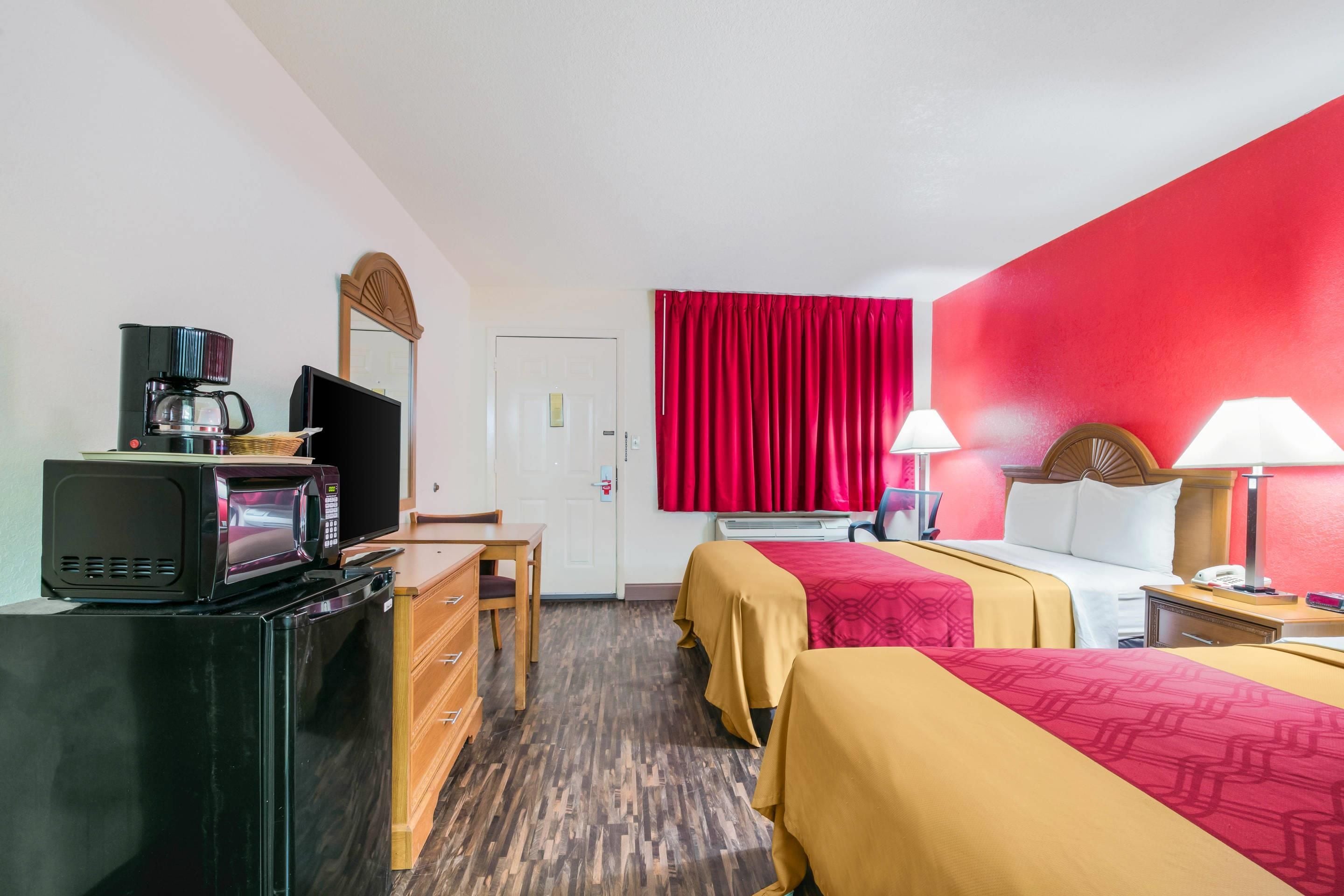 A hotel room with a bed, a desk, a television, a microwave, and a red curtain.