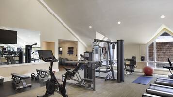 A modern gym with various exercise equipment, a large mirror, and a view of the outdoors through a large window.