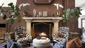 Un salon chaleureux avec une cheminée, deux fauteuils à motifs zébrés, un pouf rond et un canapé en cuir.