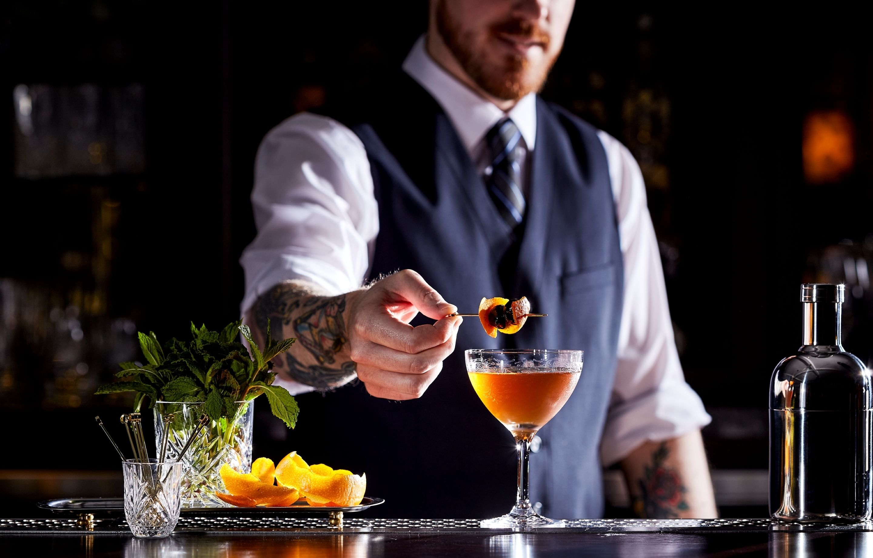 A bartender preparing a cocktail with fresh mint and orange slices.