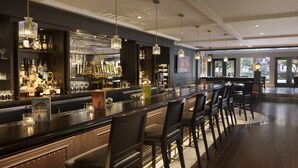 Un espace bar doté d’un long comptoir, de nombreux tabourets et de luminaires suspendus.