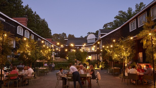 Un espace extérieur aménagé pour les repas, avec des tables et des chaises, entouré d’immeubles et d’arbres.