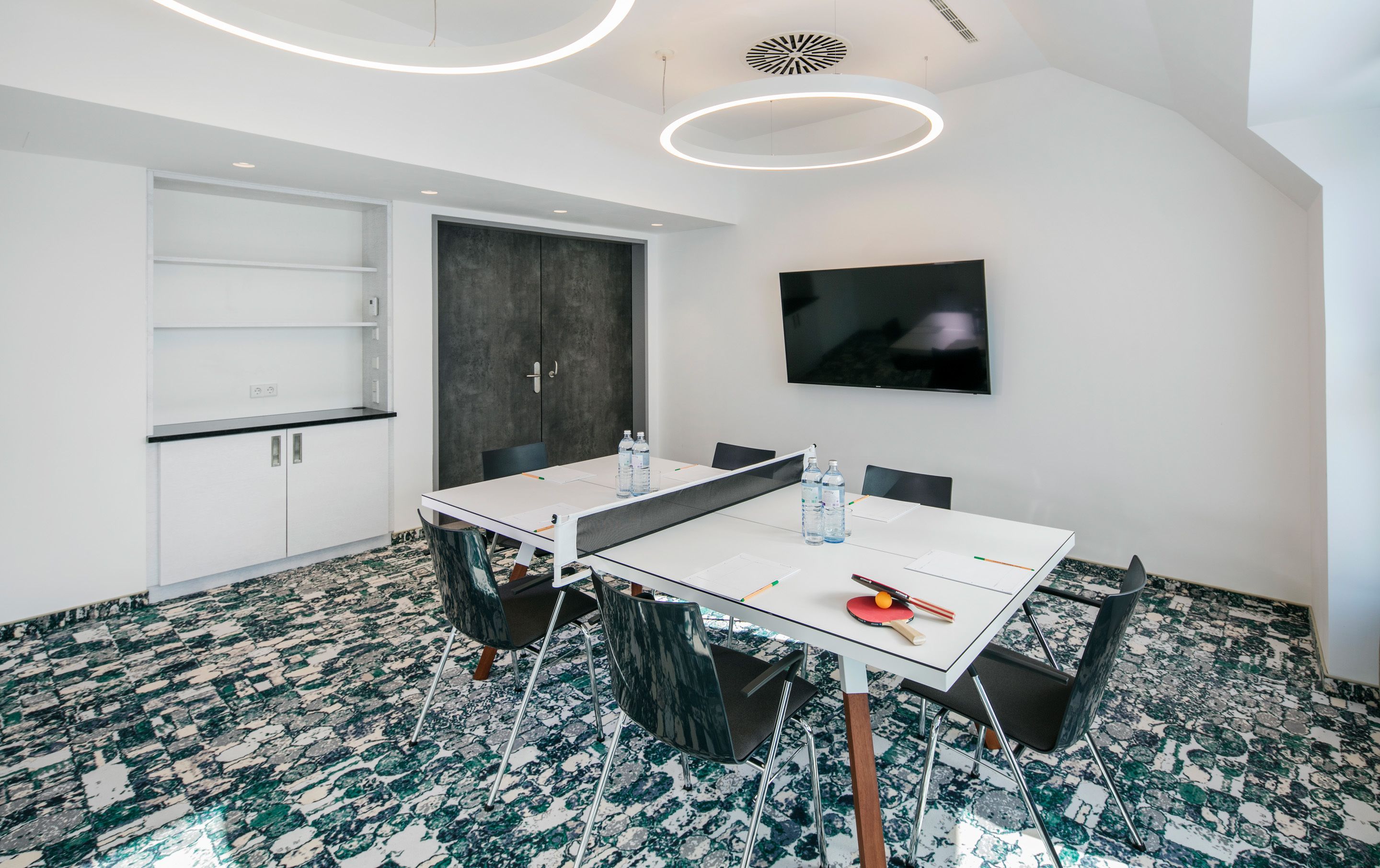 A modern conference room with a white table, black chairs, and a large screen.