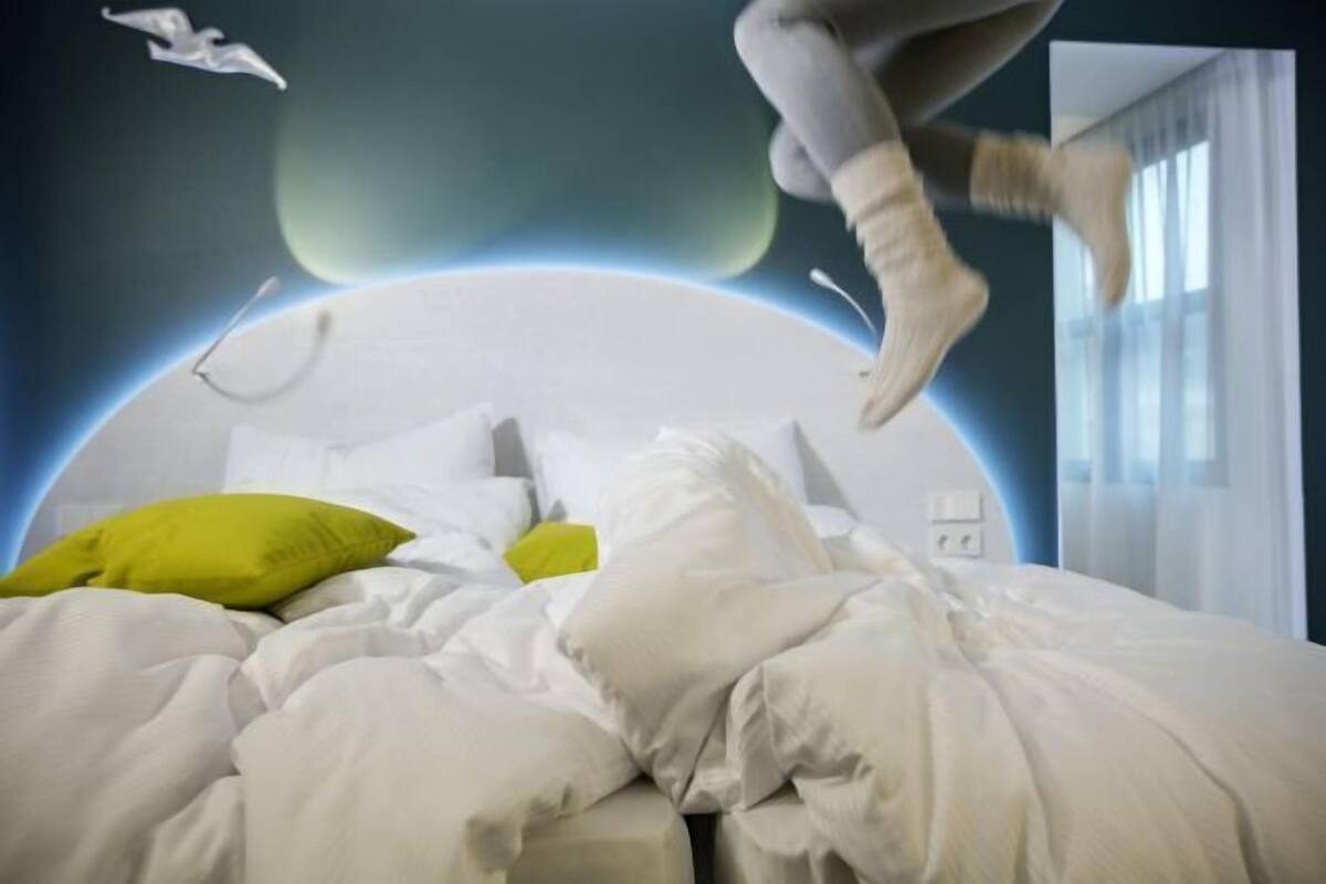 A bed with white bedding and a green pillow, a wall with a circular design, and a window with curtains.