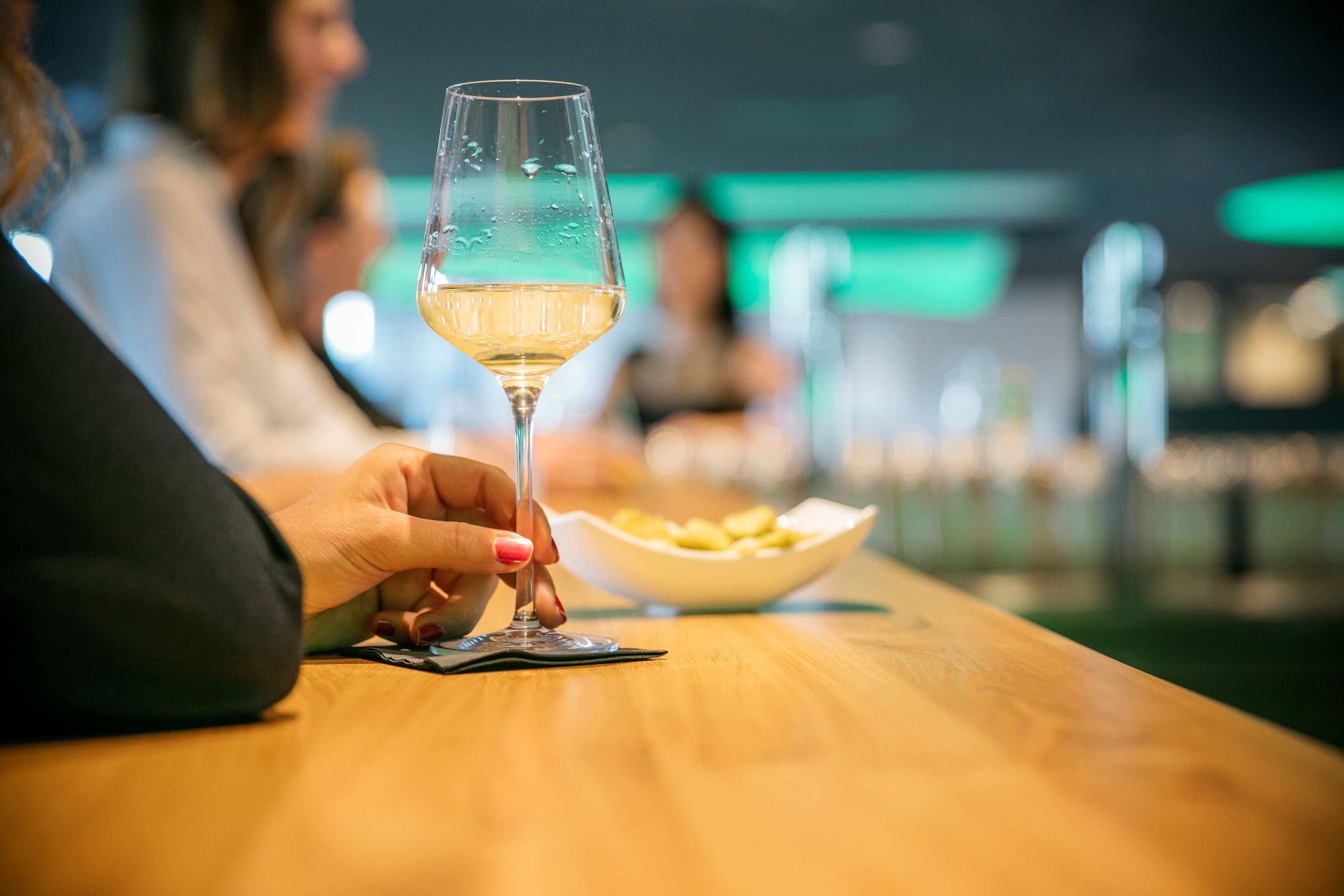 Une personne tenant un verre de vin au bar, avec un bol de collations en arrière-plan.