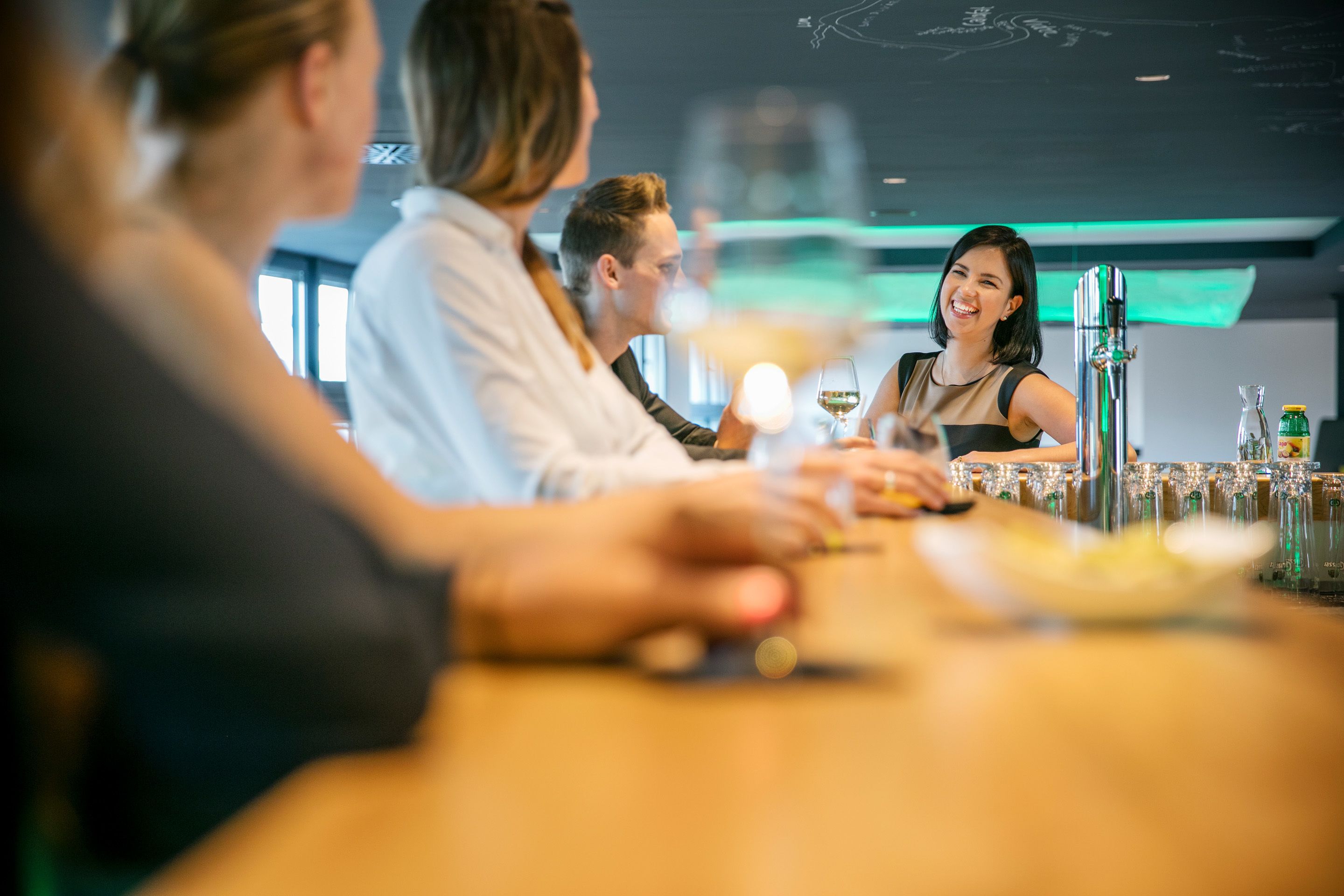 A bar setting with a bartender, a customer, and a server. There are glasses and bottles on the counter.