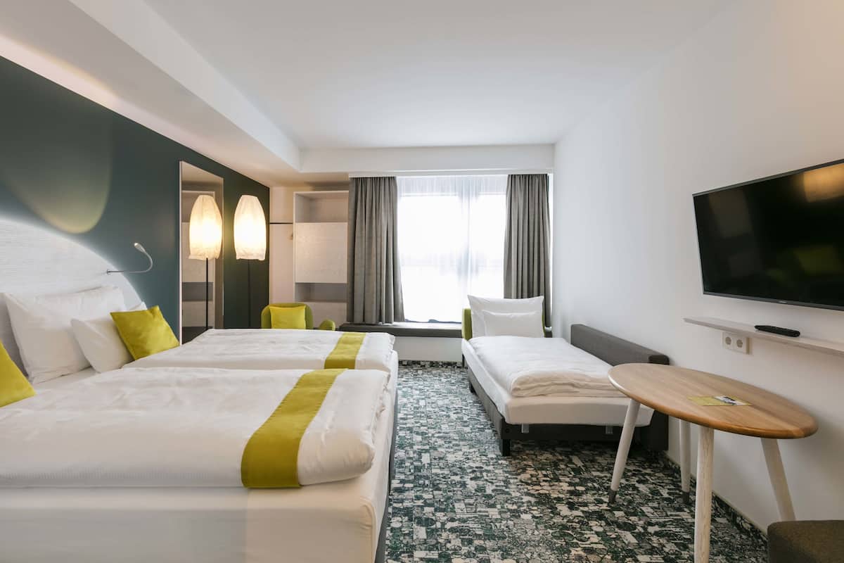 A hotel room with two beds, a TV, a small table, and a window with curtains.