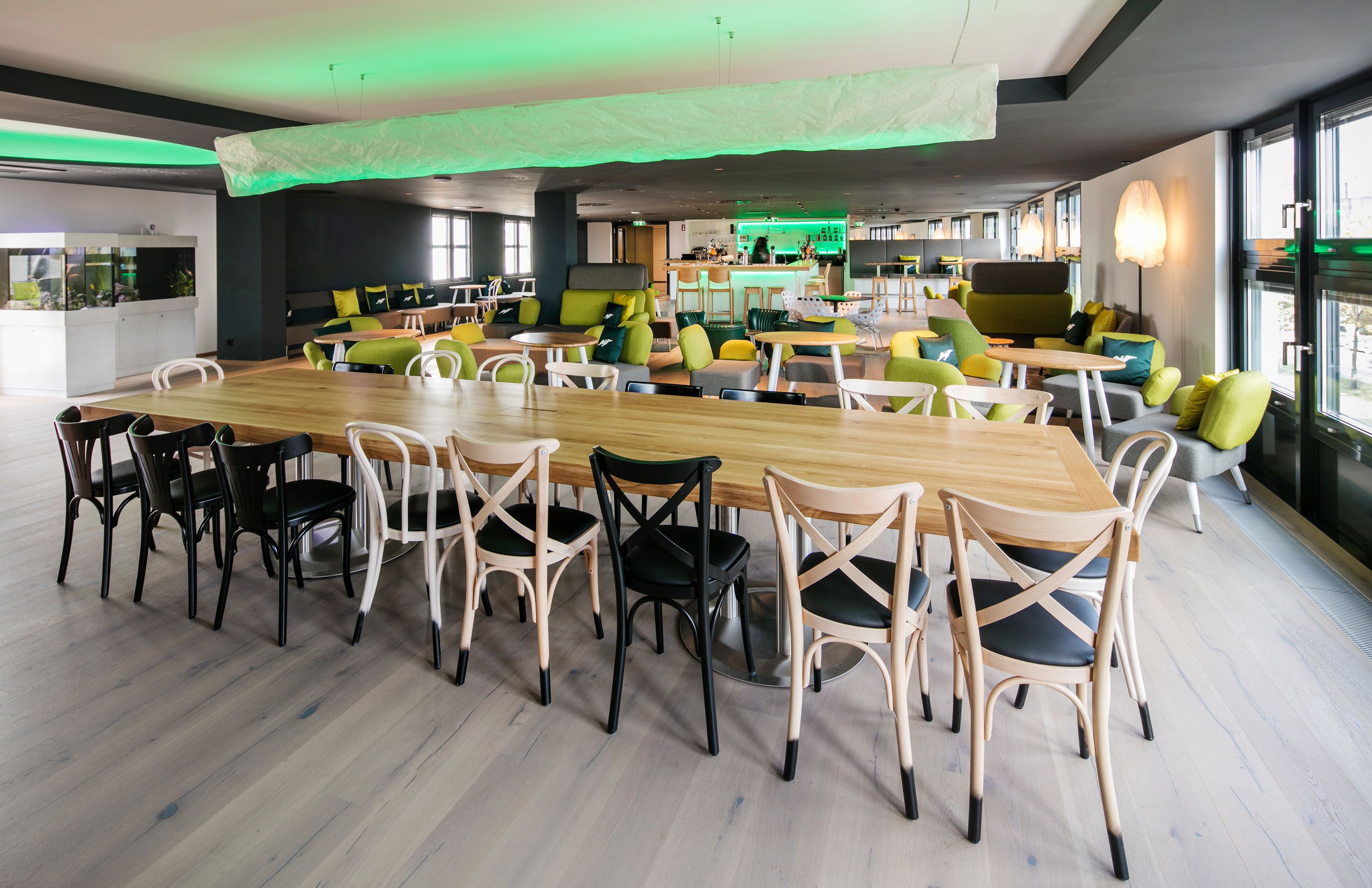 A modern dining area with a long wooden table and chairs, surrounded by green and yellow seating.