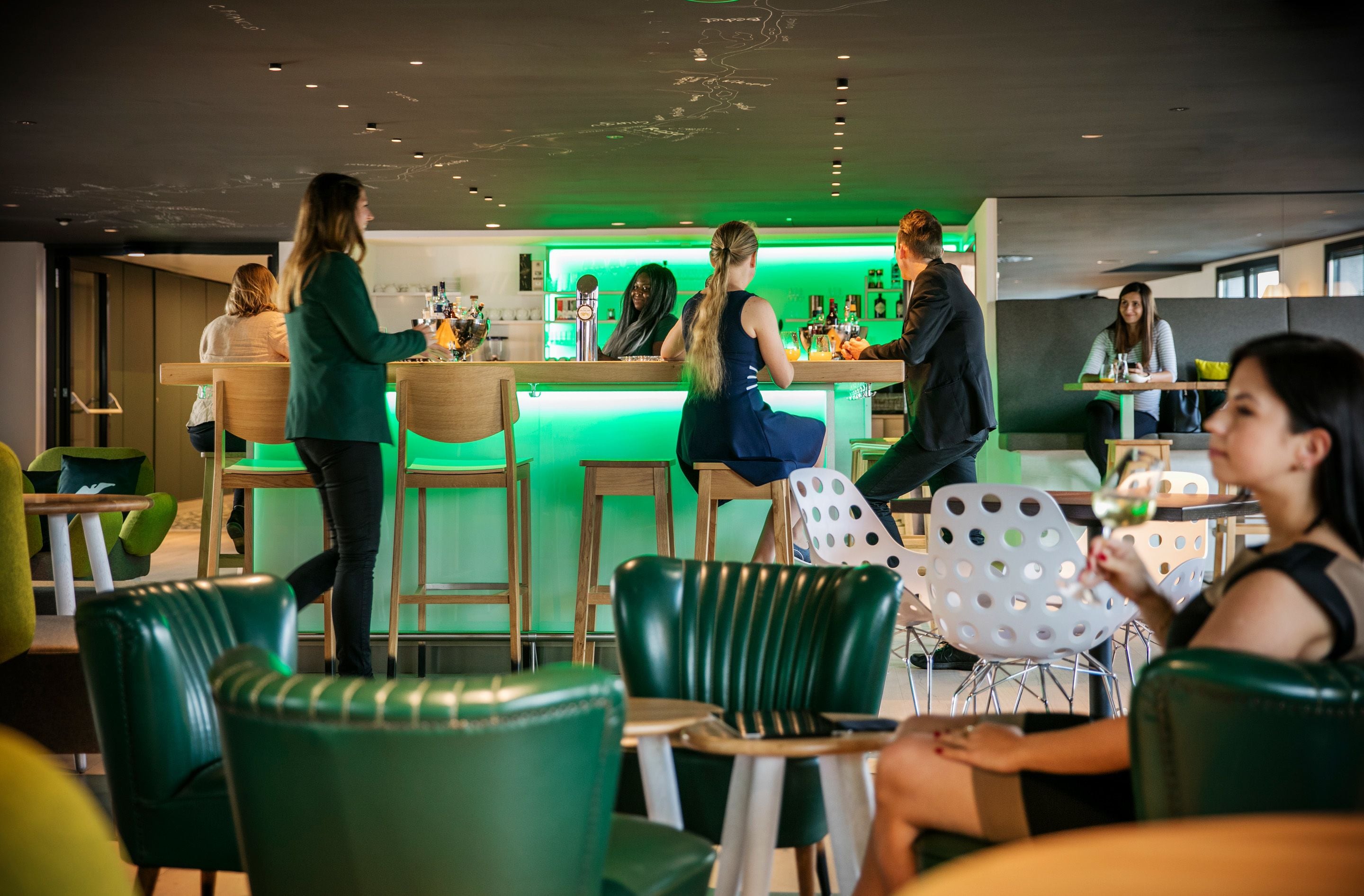 A modern bar area with green lighting, wooden furniture, and a bar counter.