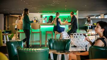A modern bar area with green lighting, wooden furniture, and a bar counter.