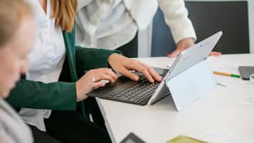 A group of people in a meeting room with laptops and documents on a table.