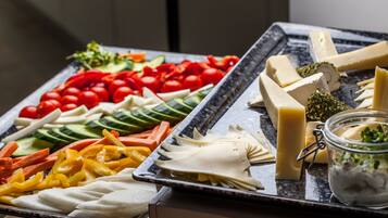 A buffet with various cheeses, vegetables, and a jar of olives.