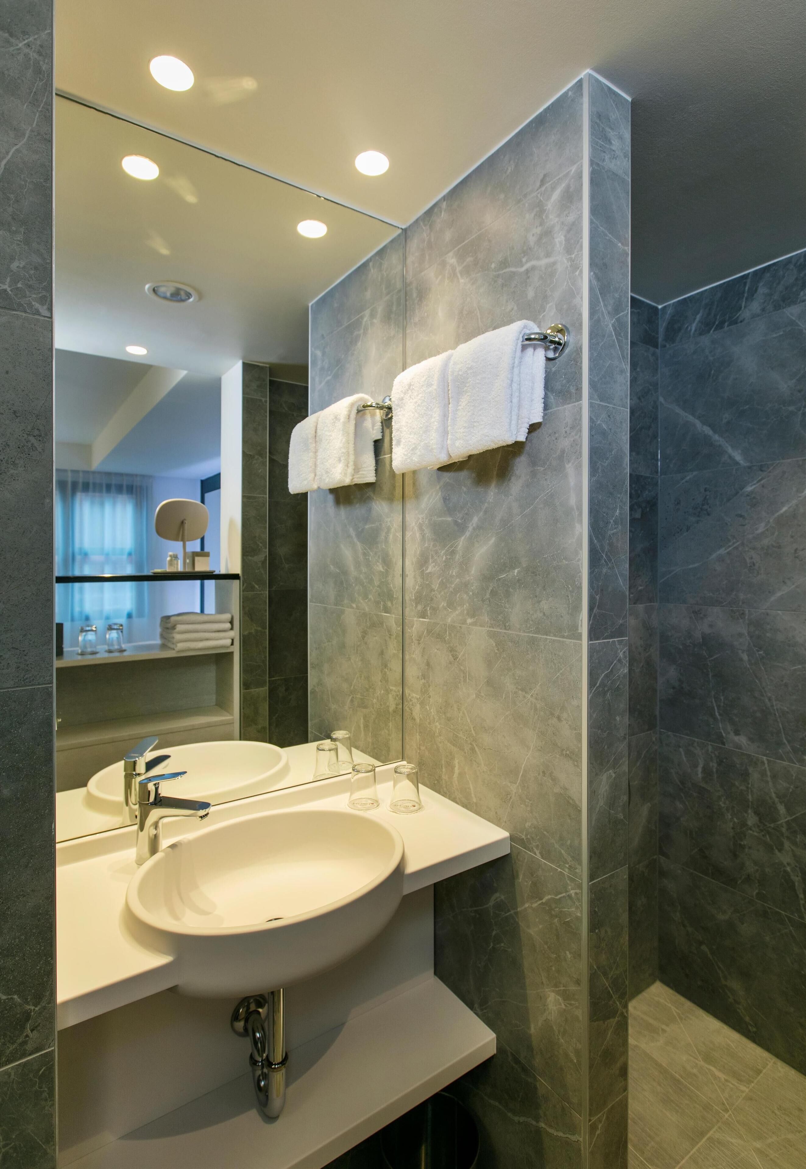 Une salle de bain moderne avec deux vasques, un grand miroir et des murs en marbre foncé.