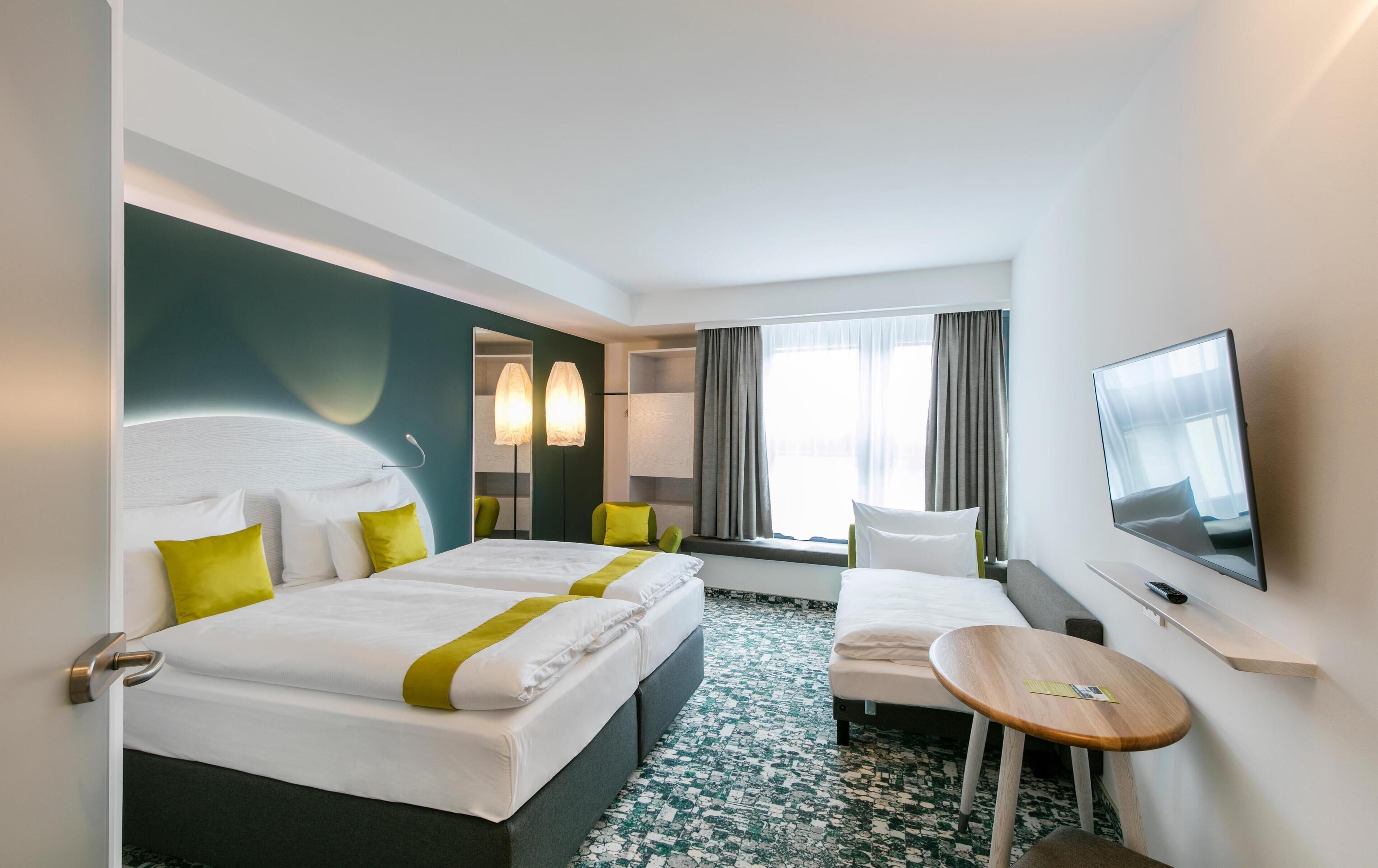Una habitación de hotel con dos camas, una mesita, un televisor y una ventana con cortinas.