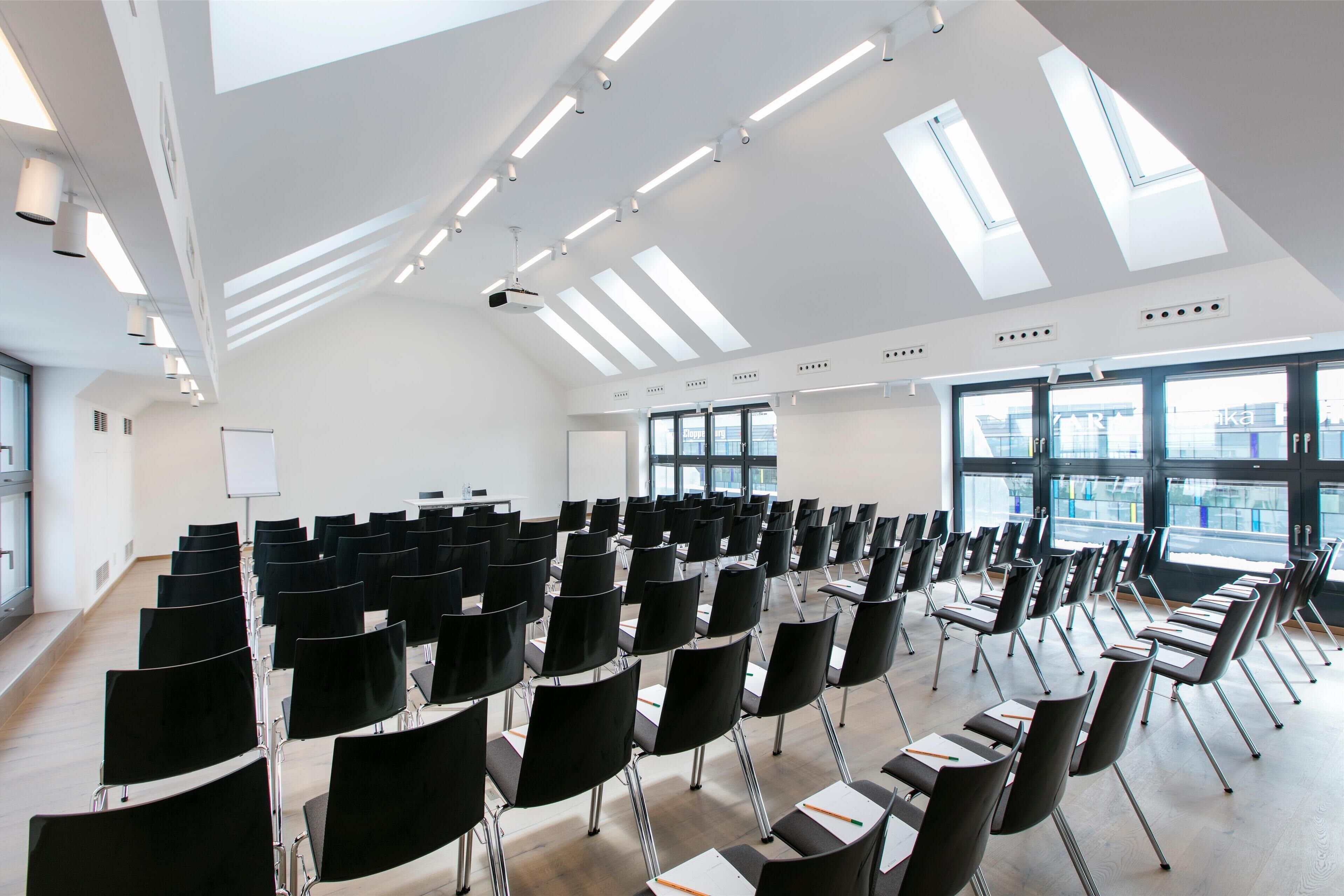A conference room with rows of black chairs, a whiteboard, and large windows with a city view.