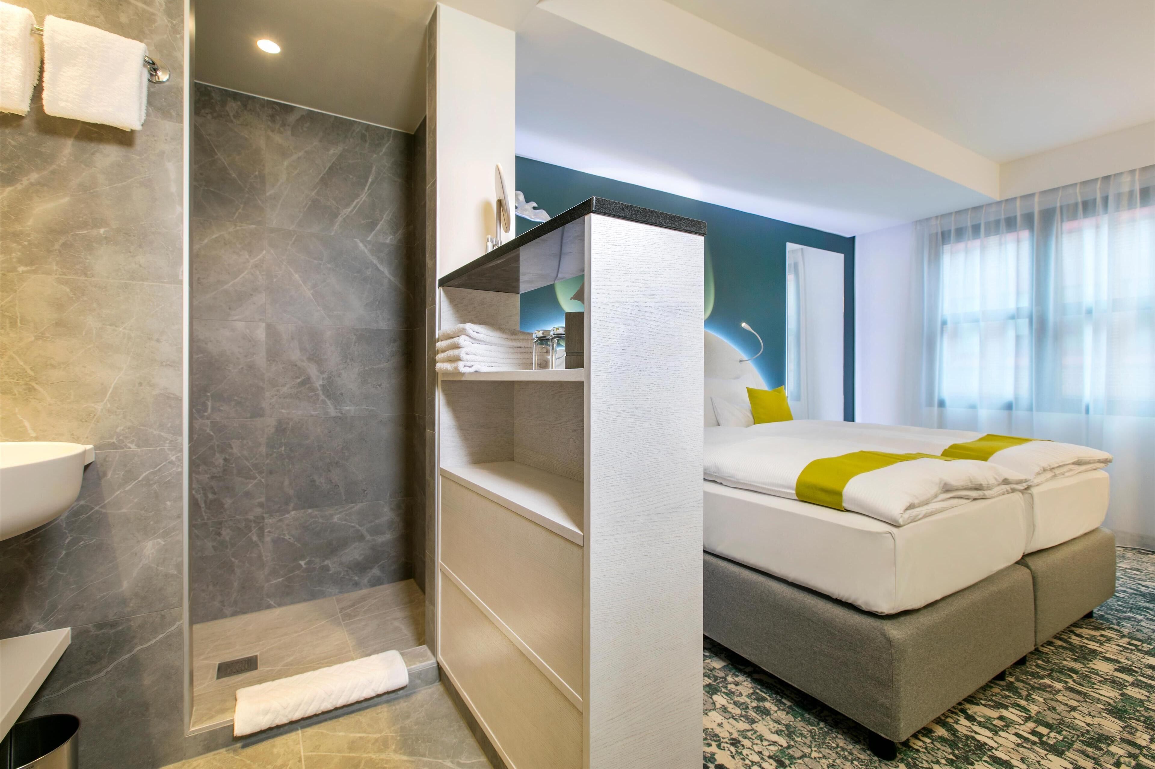 A modern hotel room with a shower, a bed with a headboard, a bedside table, and a window with curtains.