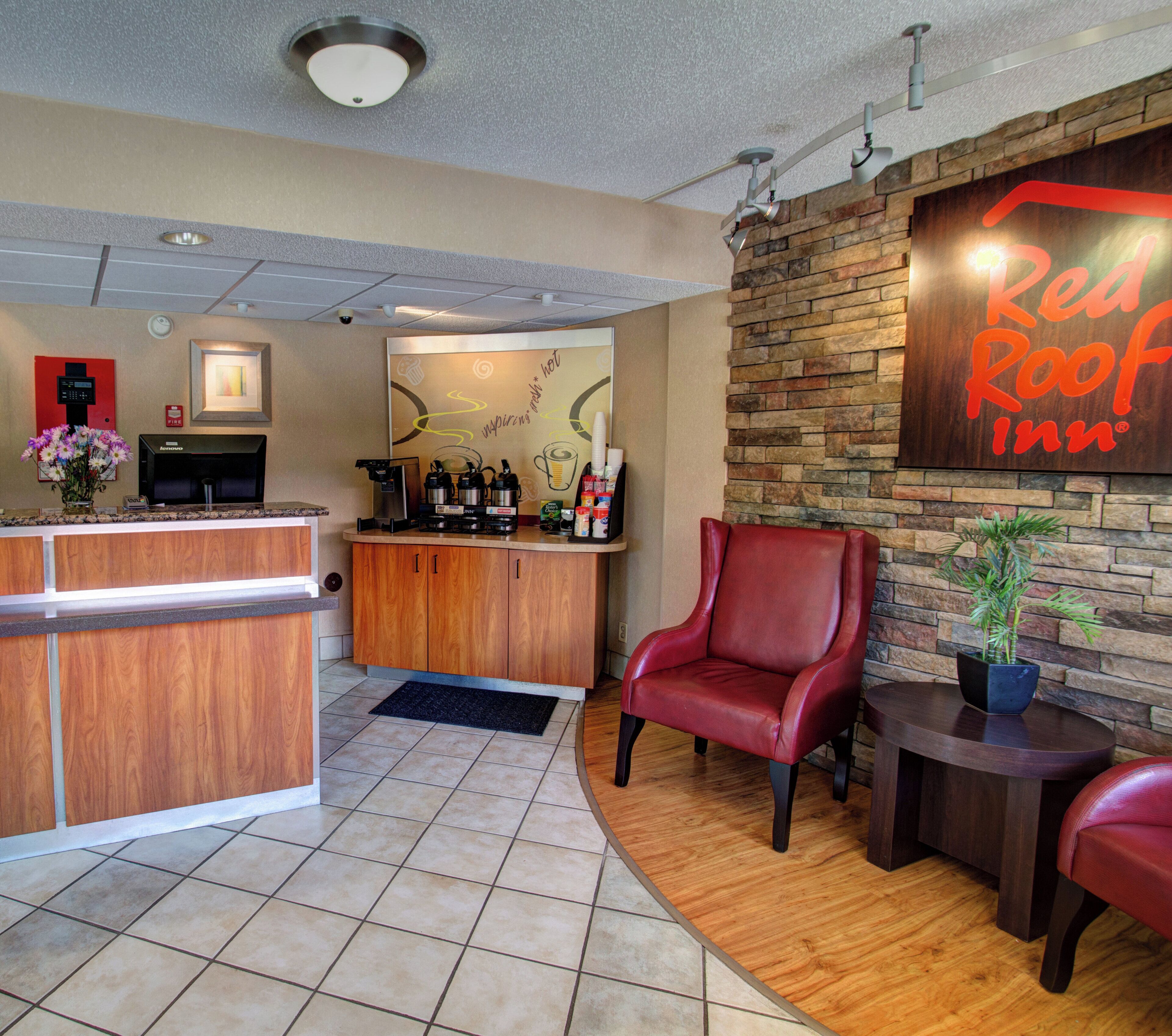 A Red Roof Inn reception area with a wooden counter, a coffee machine, and a seating area with leather chairs.
