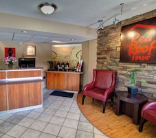 A Red Roof Inn reception area with a wooden counter, a coffee machine, and a seating area with leather chairs.