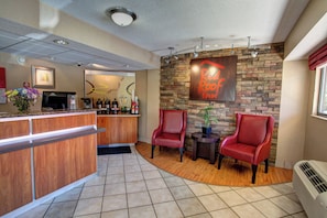 A reception area with a wooden counter, two red chairs, a small table with a plant, and a wall-mounted sign. - Red Roof Inn Pensacola – I-10 at Davis Highway (Pensacola)