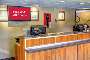 Ein Hotelrezeptionstisch mit einem roten Schild, das 'Kostenloses WLAN in allen Zimmern' anzeigt.