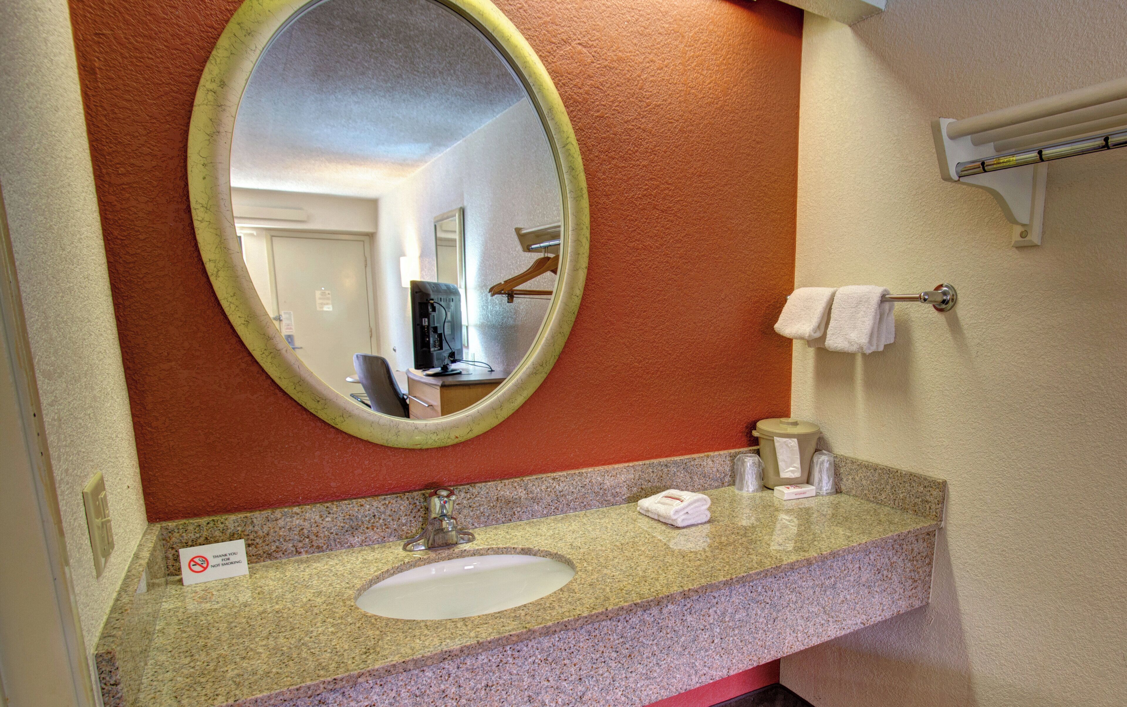 A bathroom with a granite countertop, a sink, a mirror, a towel rack, and a trash can.