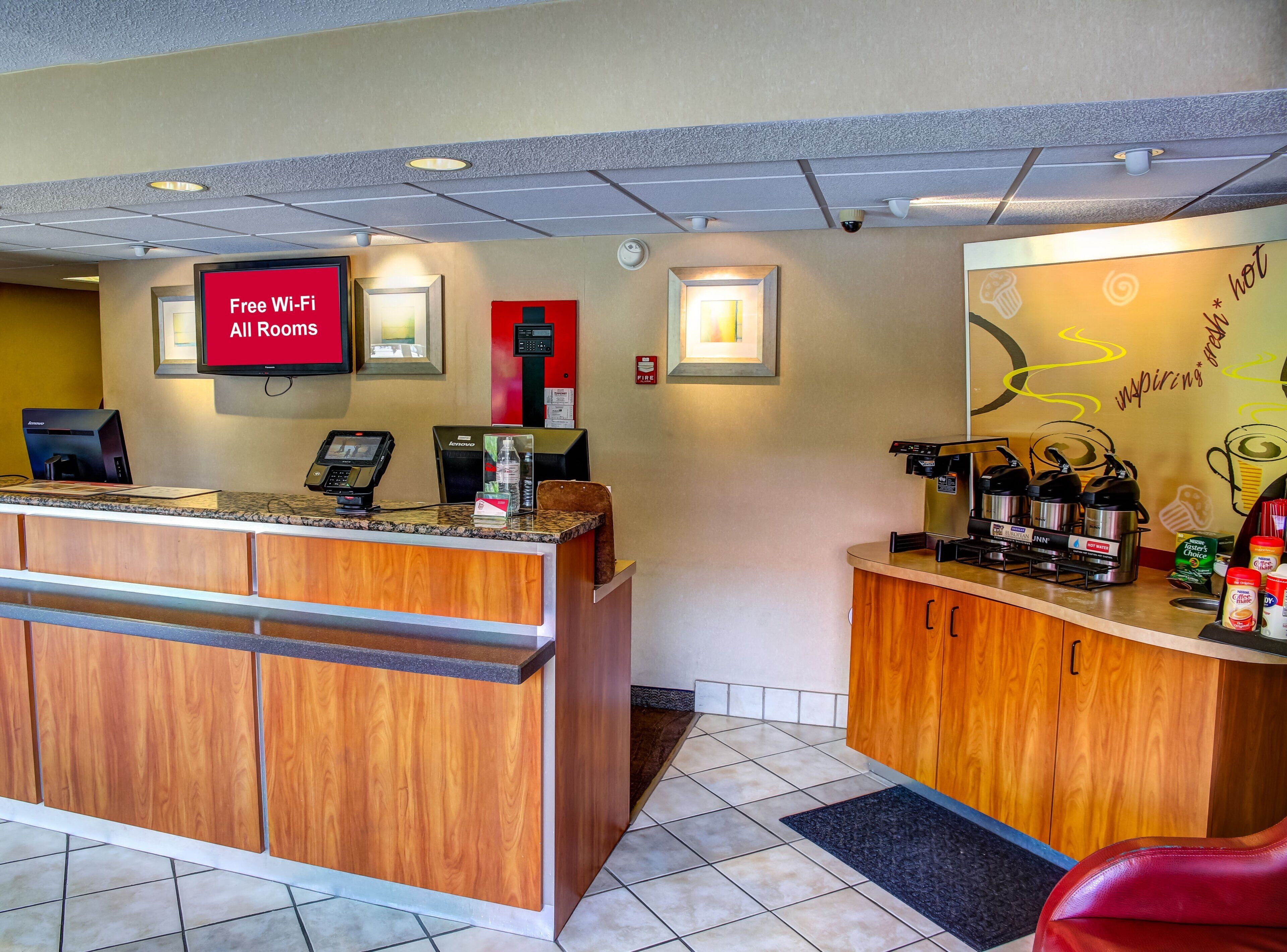 A hotel reception area with a digital screen displaying 'Free Wi-Fi All Rooms,' a coffee machine, and a water dispenser.