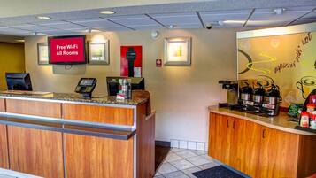 A hotel reception area with a digital screen displaying 'Free Wi-Fi All Rooms,' a coffee machine, and a water dispenser.