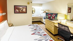 A hotel room with a bed, a desk with a computer, a television, a mirror, and a bathroom visible in the background. - Red Roof Inn Pensacola – I-10 at Davis Highway (Pensacola)