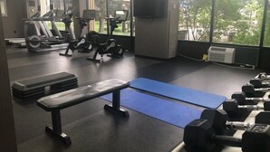 Un gimnasio con cintas de correr, bicicletas estáticas, un banco y mancuernas.