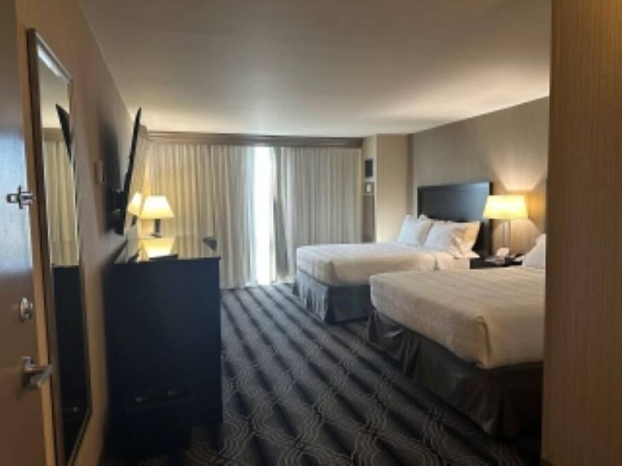 A hotel room with two beds, a large mirror, a dresser, and a window with curtains.