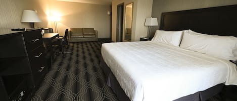 Una habitación de hotel con una cama grande, un escritorio con una silla, un sofá y un aparador.