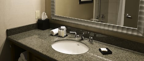 A hotel bathroom with a large mirror, a sink, and a shower. There are towels and toiletries on the counter.