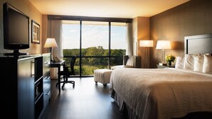 Habitación de hotel con una cama grande, un escritorio con una silla, un televisor y vistas al exterior a través de un ventanal amplio.