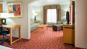 A hotel room with a red patterned carpet, a desk with a computer, a sofa, a small table, and a television. - Holiday Inn Express Grants Pass by IHG (Grants Pass)