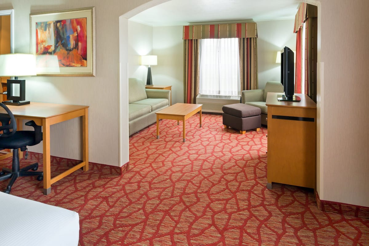 A hotel room with a red patterned carpet, a desk with a computer, a sofa, a small table, and a television.