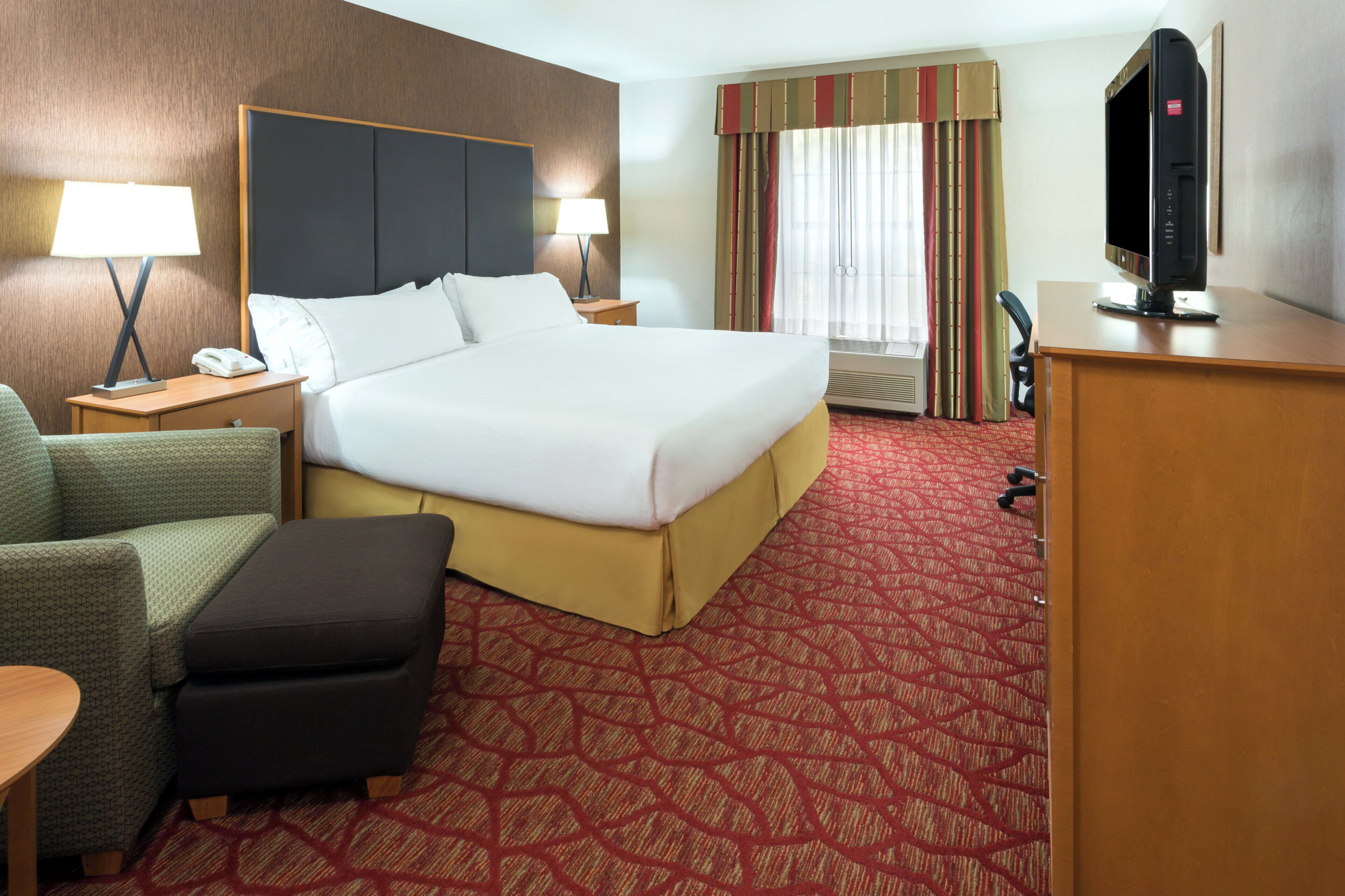 A hotel room with a large bed, a desk, a chair, a television, and a desk lamp.